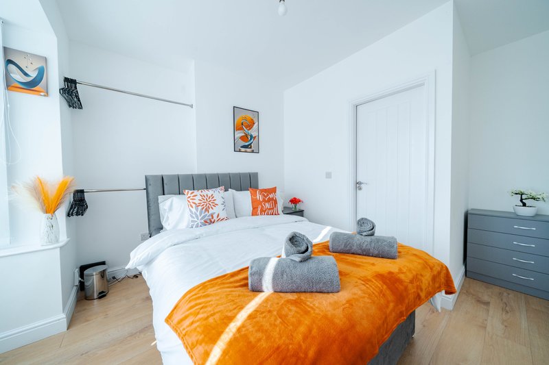 Bright modern bedroom with gray upholstered bed, orange throw blanket, white bedding, and wooden flooring