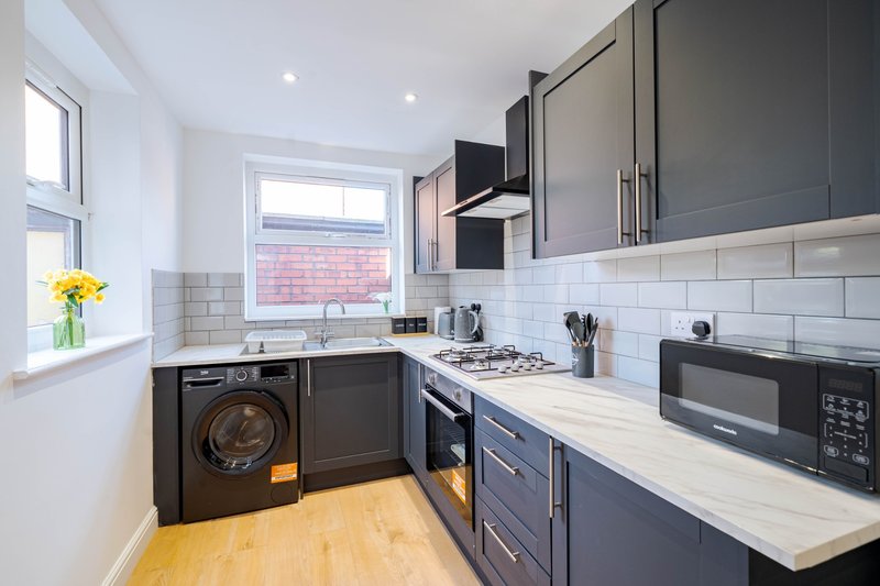 Modern kitchen with dark cabinetry, white countertops, integrated appliances and window