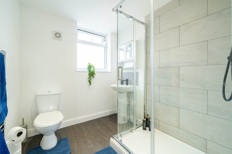 Modern bathroom with toilet, walk-in shower, window, and dark wood flooring