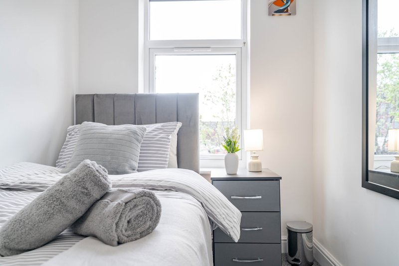 Bright bedroom with double bed, gray upholstered headboard, and bedside table with window