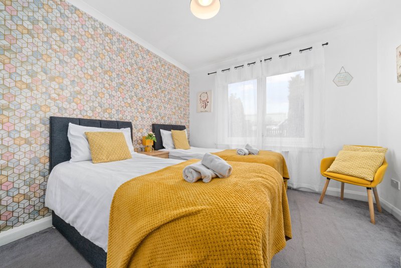 Bright bedroom with two twin beds, yellow bedding, geometric wallpaper accent wall and window