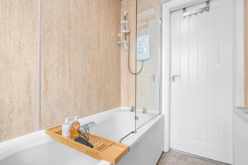 Modern bathroom with white bathtub, glass shower screen, wooden bath caddy and beige tile walls