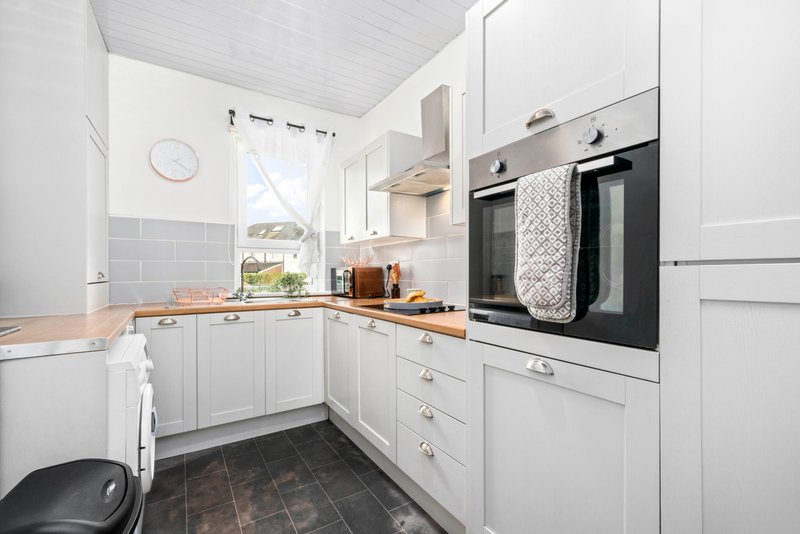 Modern white kitchen with built-in oven, wooden countertop, and window overlooking garden