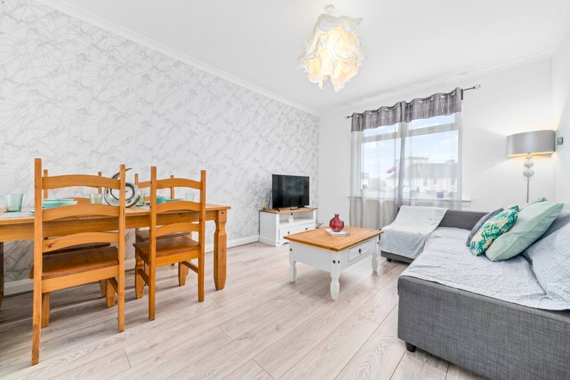 Open-plan living room with wooden dining table, sofa bed, TV and bright windows