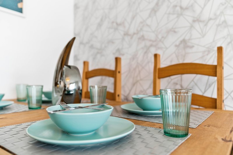 Dining table set with turquoise bowls, wooden chairs, and marble wall backdrop