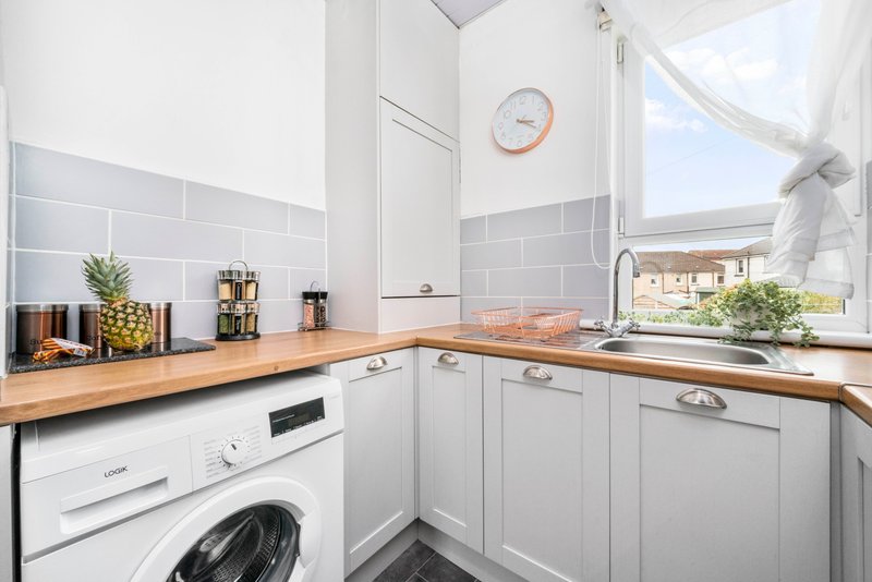 Modern white kitchen with wooden countertop, integrated appliances, and window overlooking garden