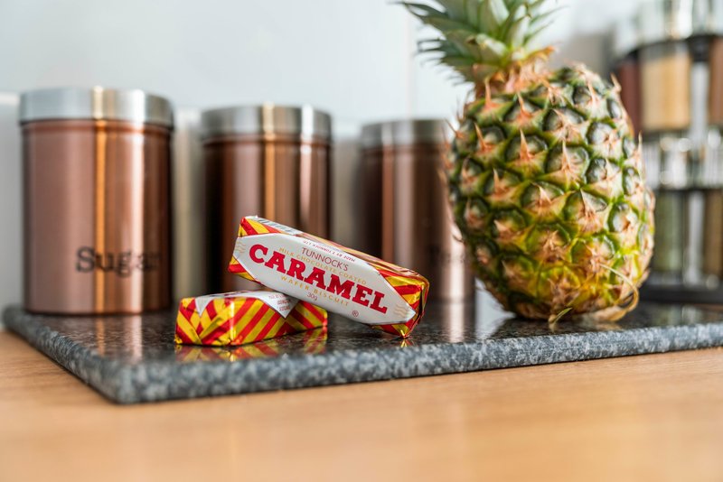 Kitchen counter with metallic storage containers, fresh pineapple, and caramel sweets on a grey mat