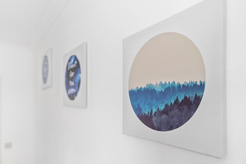 White bedroom wall with three framed landscape artworks featuring forest and mountain scenes