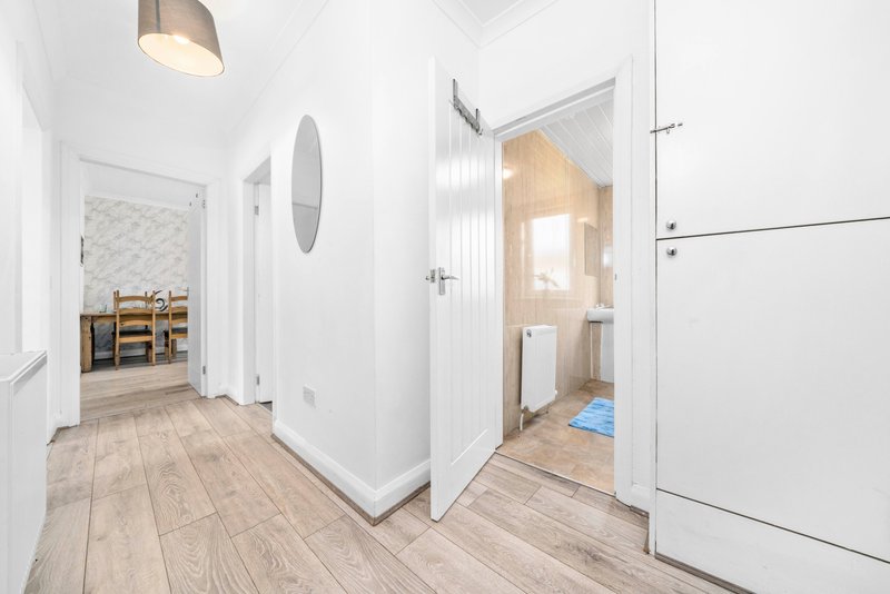 Bright hallway with wooden flooring, white walls, pendant light and multiple doors