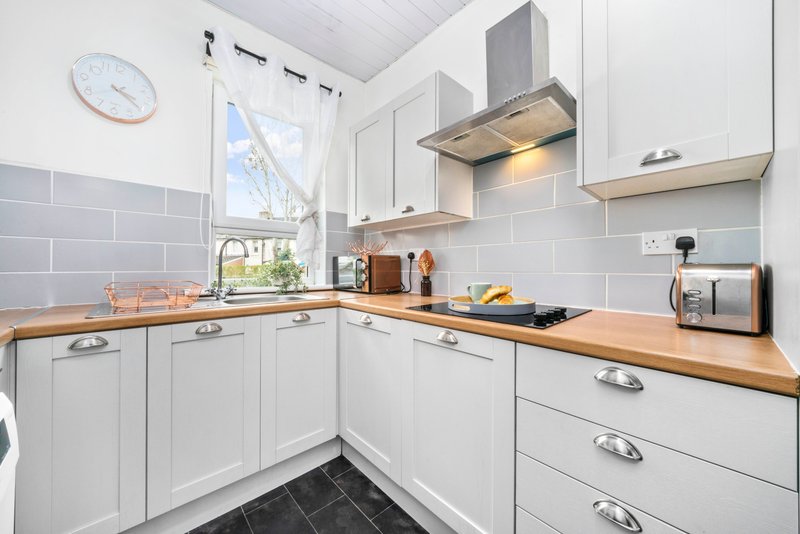 Modern white kitchen with wooden countertops, gas hob, extractor hood and grey tile splashback