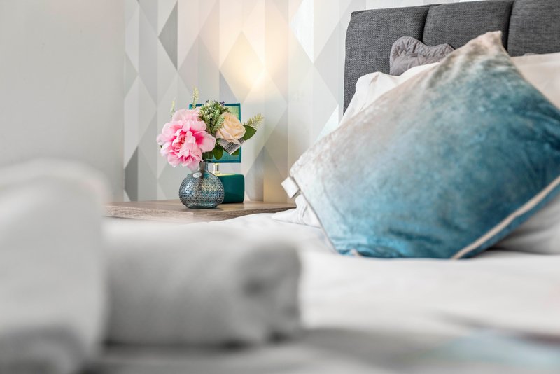 Modern bedroom with grey upholstered headboard, blue cushion, white bedding and floral bedside arrangement