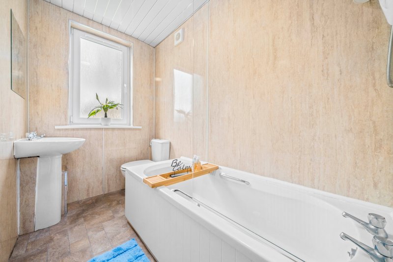 Bathroom with bathtub, pedestal sink, window, and beige tile walls