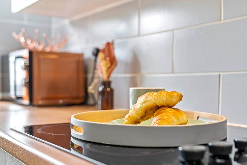 Modern kitchen countertop with croissants in a bowl, toaster, and white subway tile backsplash