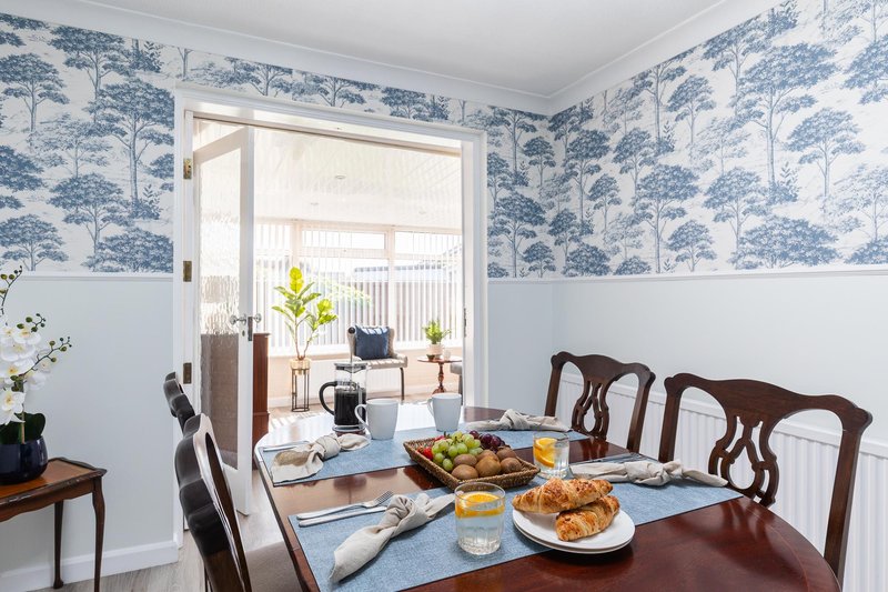 Dining room with wooden table, chairs, blue toile wallpaper, and French doors to garden