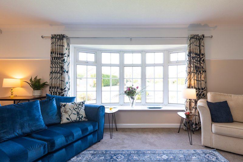 Bright living room with blue sofa, cream armchair, large bay window and patterned curtains