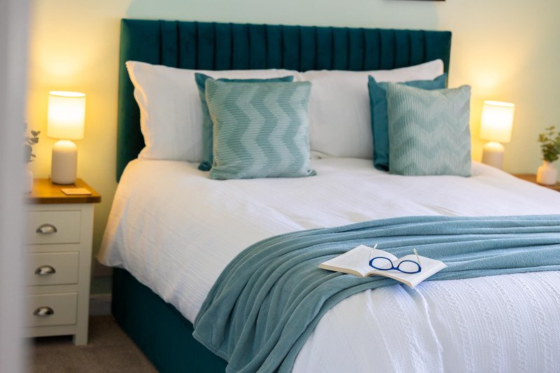 Modern bedroom with teal upholstered headboard, white bedding, patterned cushions, and bedside lamps