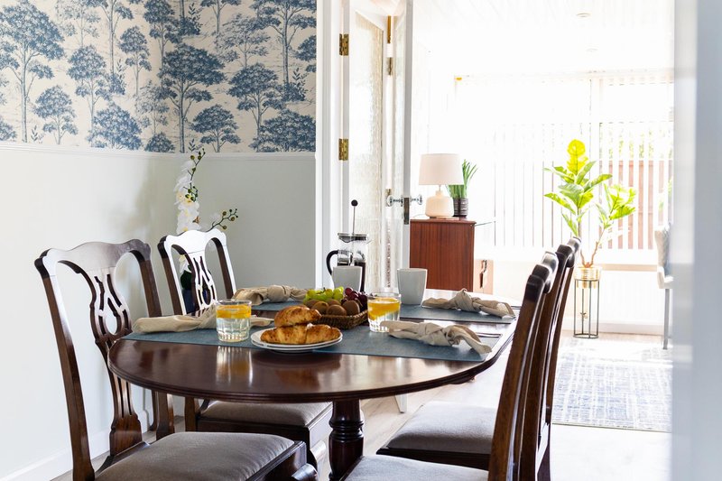 Dining room with oval dark wood table, upholstered chairs, and patterned wallpaper above dado rail