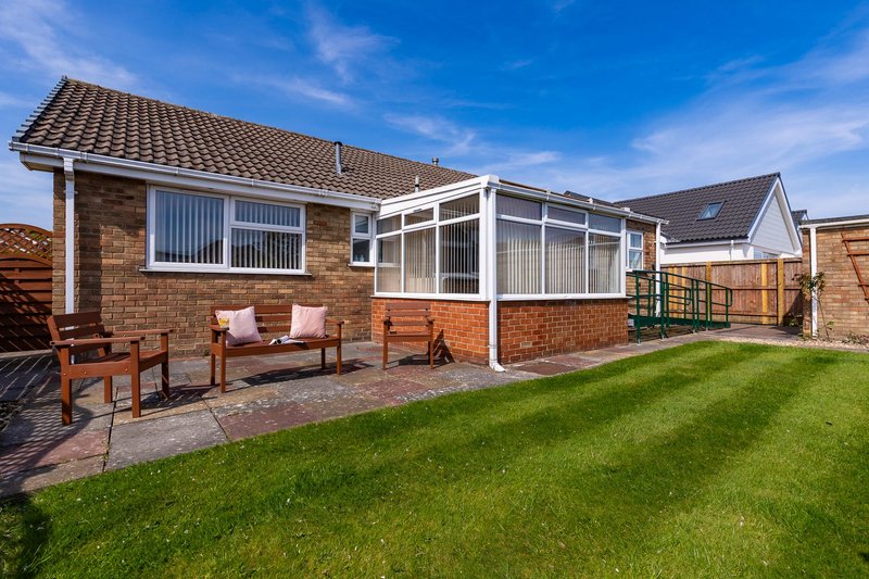Brick bungalow with conservatory, patio seating area and manicured lawn garden
