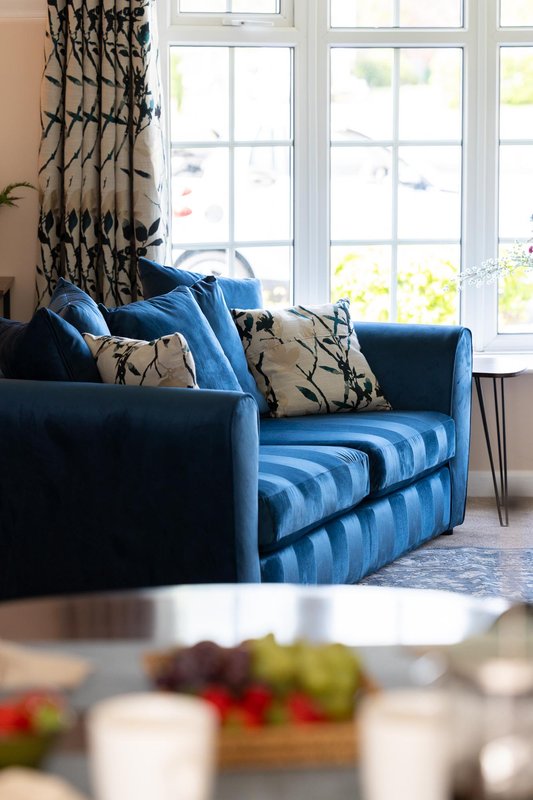 Living room with blue upholstered sofa, patterned cushions, and large windows overlooking garden