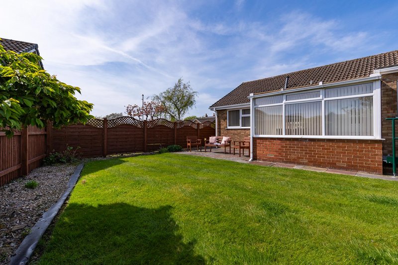Brick bungalow with conservatory, manicured garden lawn and wooden fence