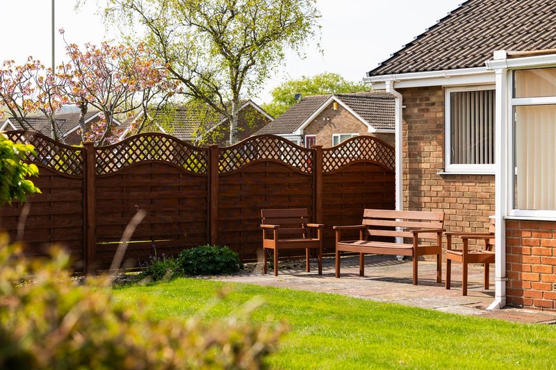 Brick house with wooden patio, garden furniture, and wooden fence surrounding landscaped garden
