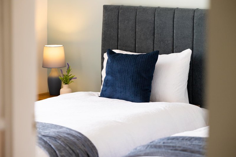 Modern bedroom with grey upholstered headboard, white bedding, navy and white pillows, and bedside lamp