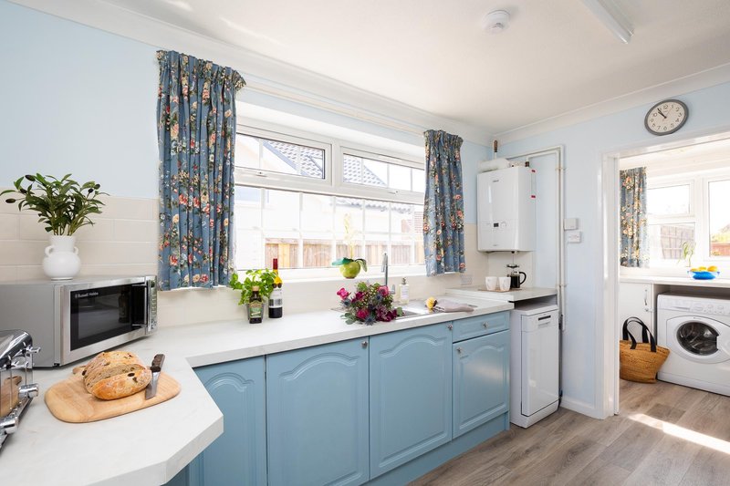 Modern kitchen with blue cabinets, white countertops, window with blue curtains and plants