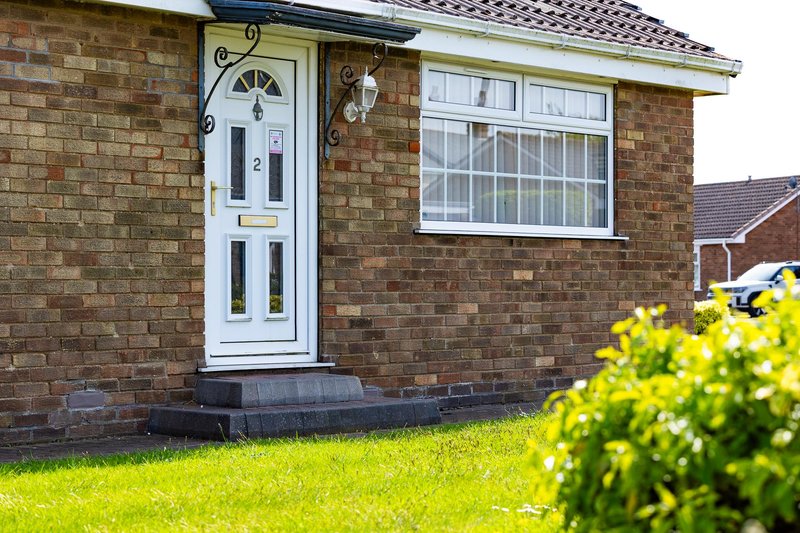 Brick bungalow exterior with white entrance door, window, and front garden