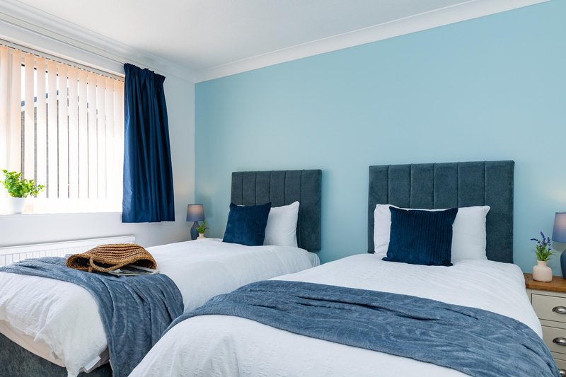 Bright bedroom with two twin beds, blue headboards, white bedding and blue accents