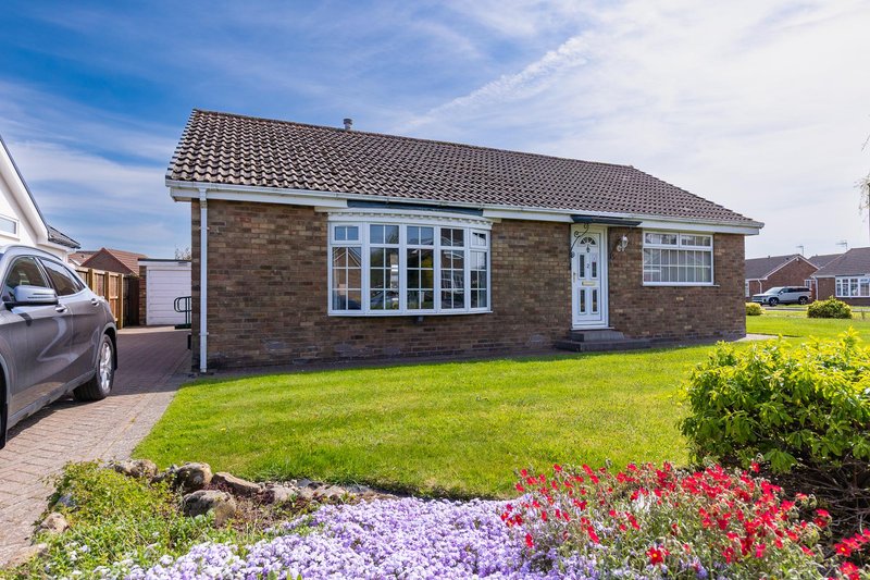 Single-story brick bungalow with driveway, manicured front garden, and colorful flower beds