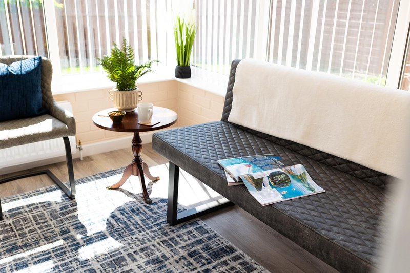 Bright living room with upholstered seating, round side table, potted plants and vertical blinds