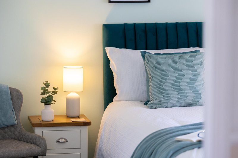 Modern bedroom with teal upholstered headboard, white bedding, and bedside lamp