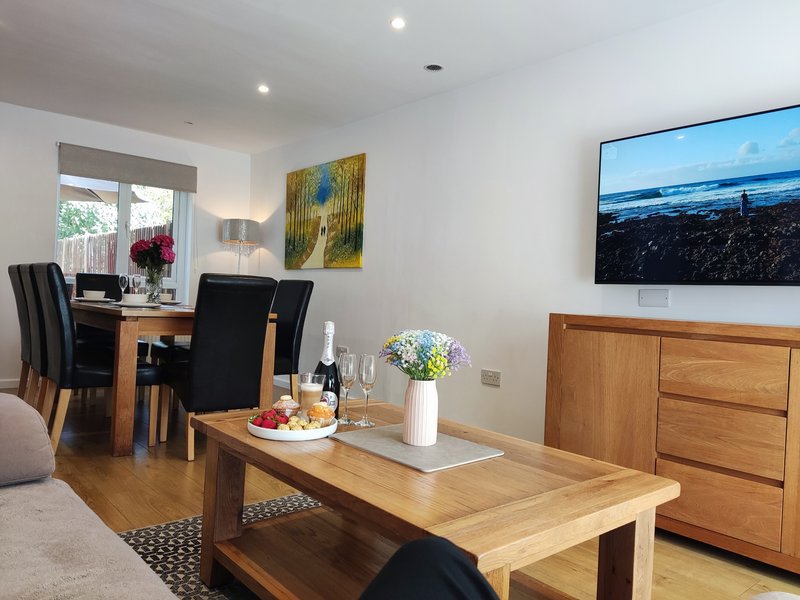 Open-plan living and dining area with wooden furniture, dining table set for two, and wall-mounted TV