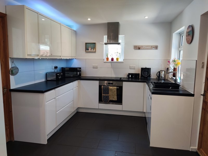 Modern kitchen with white cabinetry, black countertops, blue backsplash and stainless steel appliances