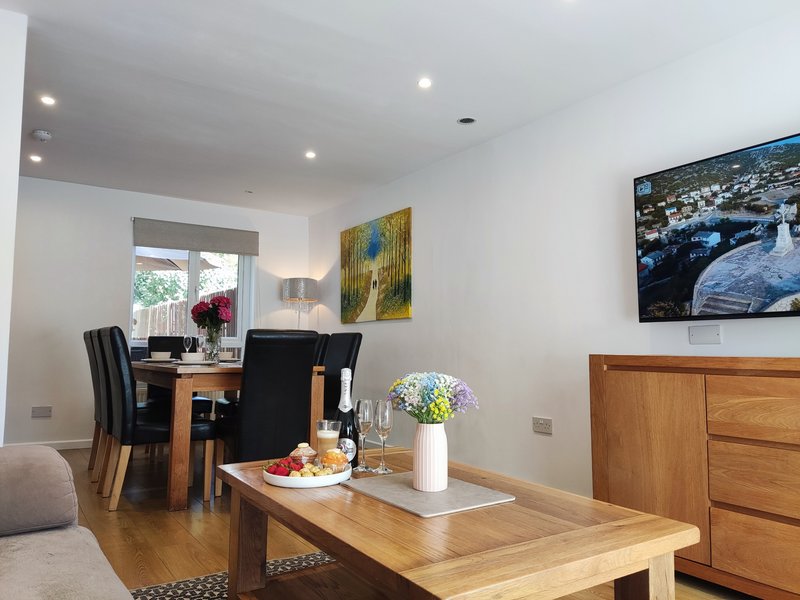 Open-plan living and dining area with wooden table, desk, framed artwork and potted flowers