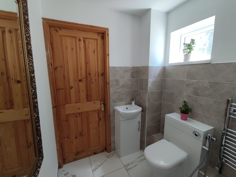 Bathroom with toilet, pedestal sink, bathtub, wooden door and tiled walls