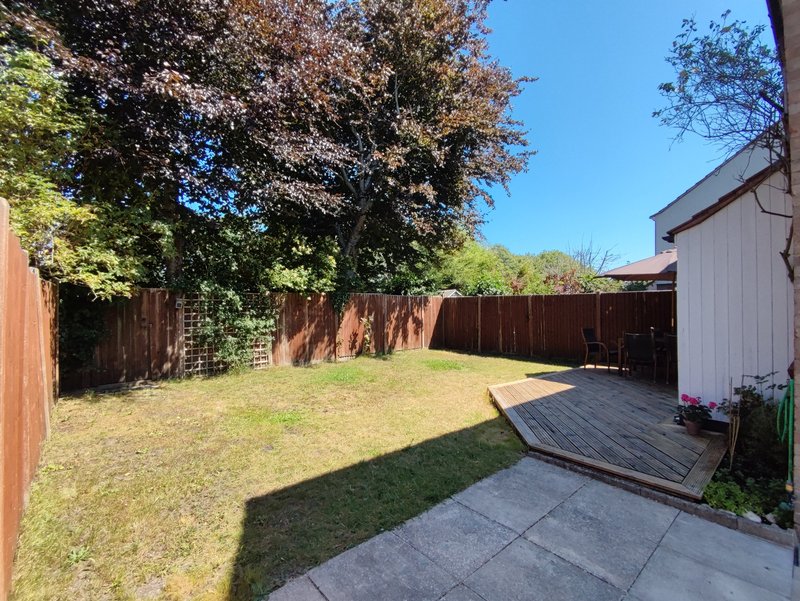 Spacious backyard with wooden fence, mature trees, paved patio and lawn area