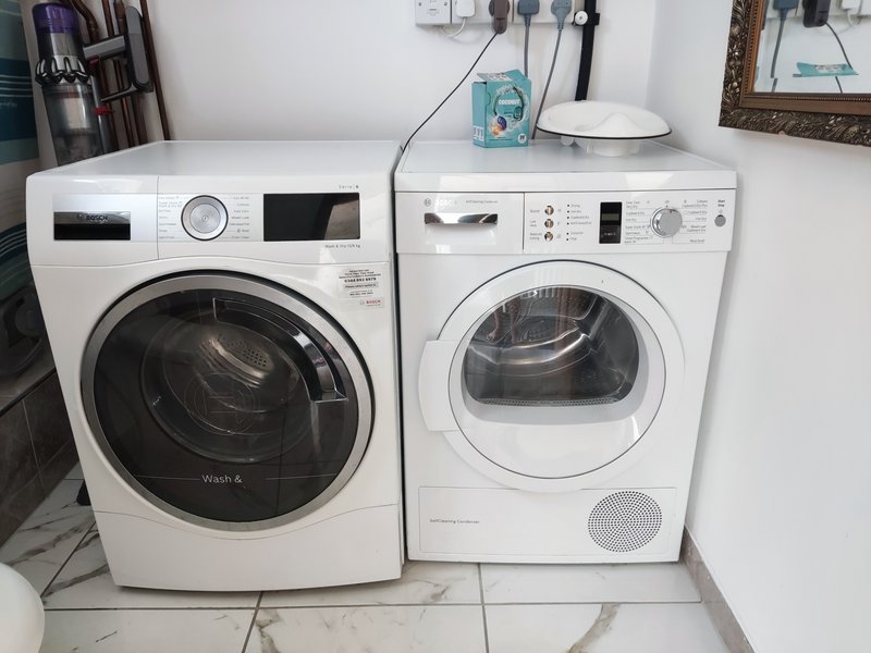 Laundry room with white washing machine and tumble dryer, tile flooring and wall-mounted storage.