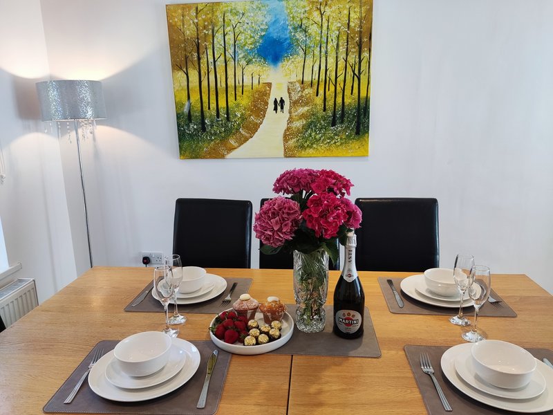 Wooden dining table set for two with place settings, flowers, wine bottle and fruit bowl