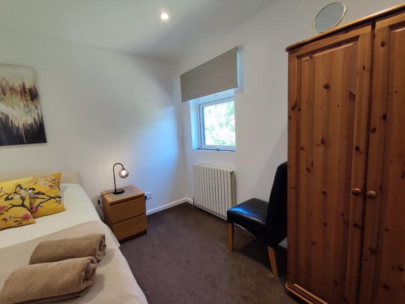 Bedroom with single bed, wooden wardrobe, desk chair and window with radiator