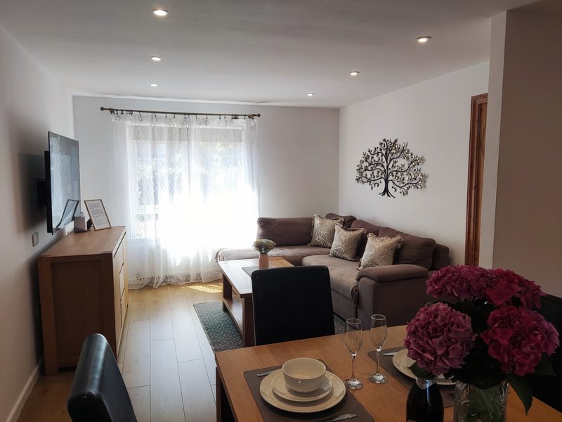 Living room with brown sofa, wooden dining table, wall-mounted TV, and decorative tree artwork