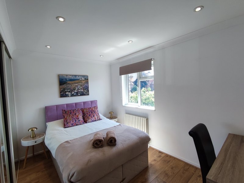 Bright bedroom with purple headboard, double bed, wooden floor and window