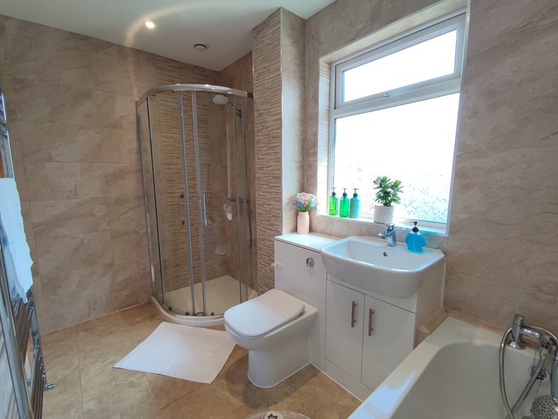 Modern bathroom with corner shower enclosure, white vanity, toilet, and large window with sill