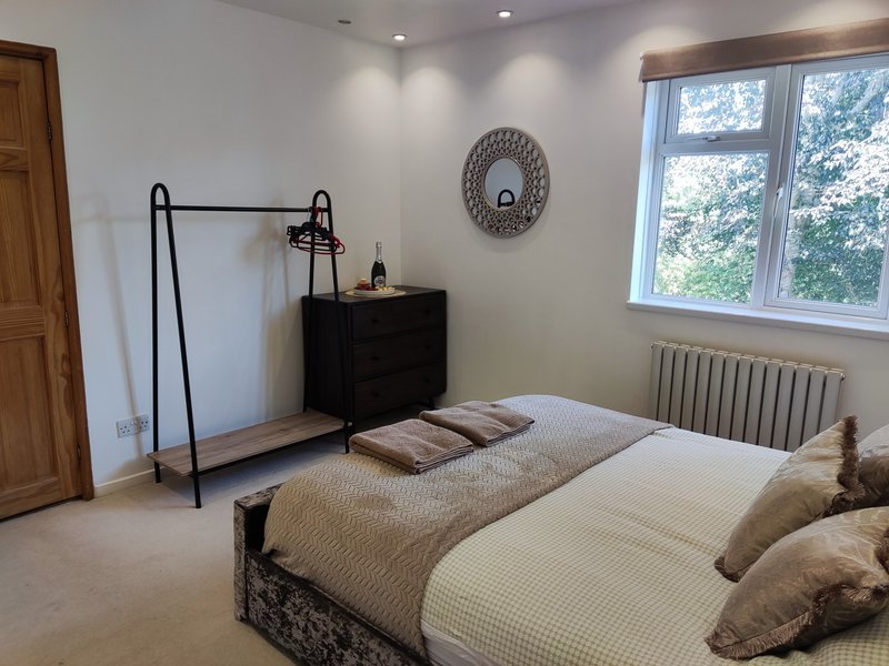 Bright bedroom with double bed, black clothing rack, wooden door and large window overlooking garden