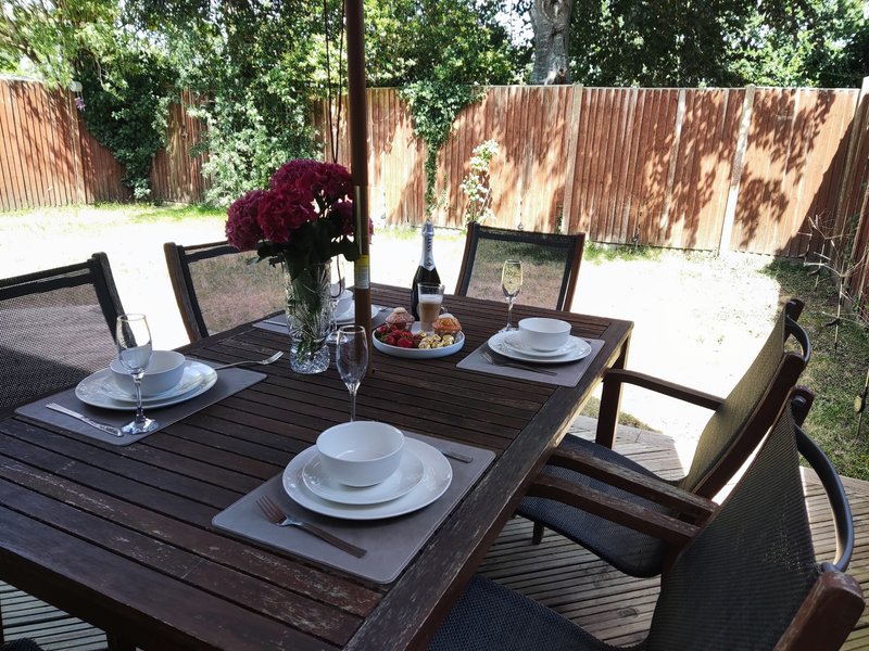 Outdoor dining table set with place settings, wine bottle, and flowers in garden with wooden fencing