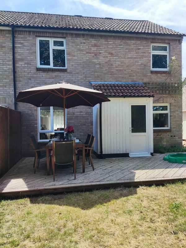 Brick house exterior with patio, dining table, black umbrella and garden area