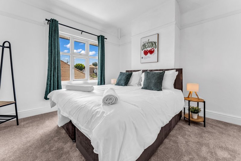 Bright bedroom with double bed, white bedding, dark headboard, green curtains and window view