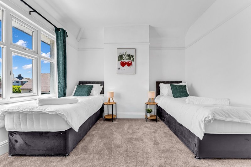 Bright twin bedroom with two single beds, wooden nightstands, green curtains and window view