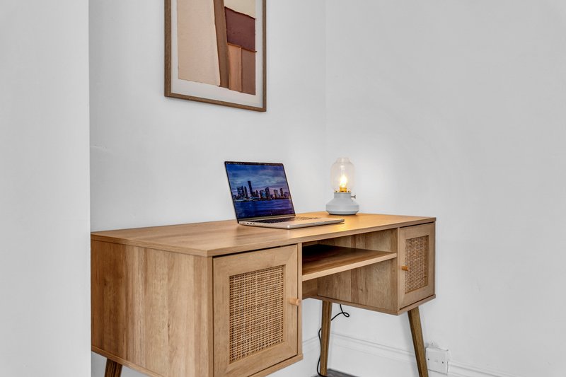 Wooden desk with laptop, desk lamp, and framed abstract art on wall above