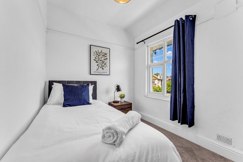 Compact bedroom with single bed, white bedding, navy pillows, wooden nightstand and window with blue curtains